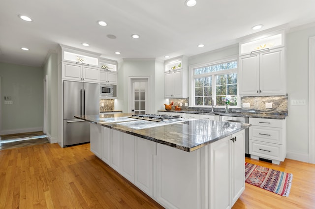 kitchen with built in appliances, a kitchen island, white cabinets, and light hardwood / wood-style floors