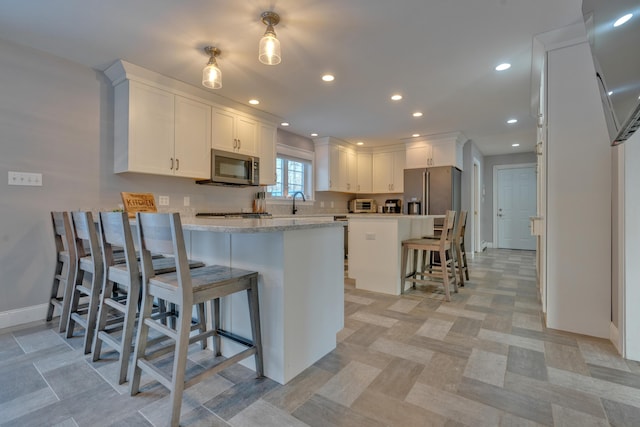 kitchen with appliances with stainless steel finishes, light stone countertops, kitchen peninsula, a breakfast bar, and white cabinetry