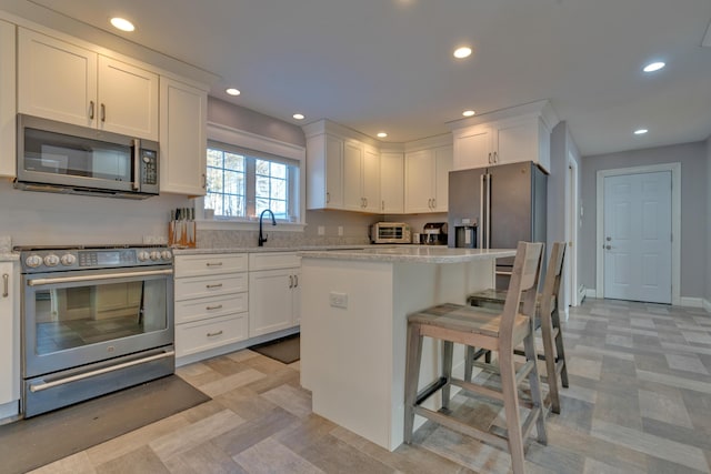 kitchen featuring light stone countertops, a center island, stainless steel appliances, white cabinets, and a kitchen breakfast bar