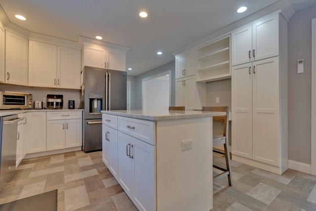 kitchen featuring stainless steel appliances, white cabinets, light stone countertops, a kitchen island, and a breakfast bar