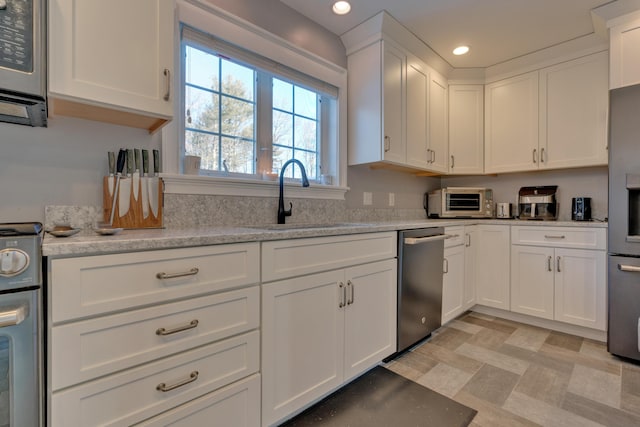 kitchen with sink, stainless steel appliances, white cabinetry, and light stone counters