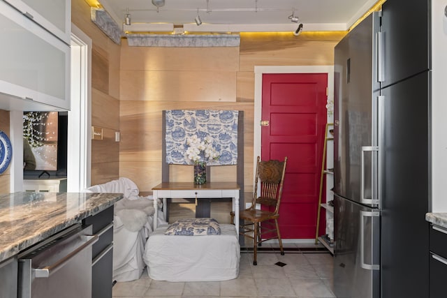 kitchen featuring stainless steel fridge, track lighting, light tile patterned floors, and wooden walls