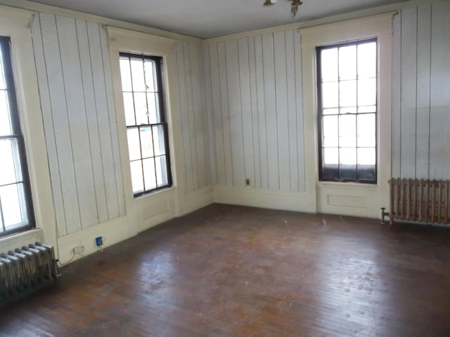 unfurnished room with dark wood-type flooring, radiator heating unit, and wooden walls