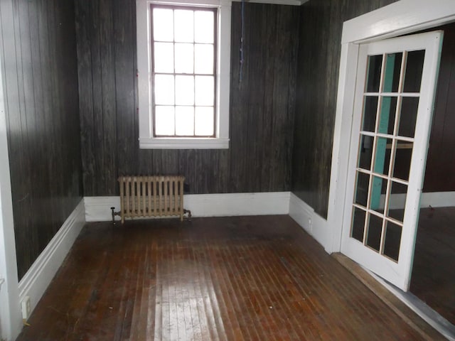 spare room with wooden walls, a healthy amount of sunlight, dark hardwood / wood-style floors, and radiator