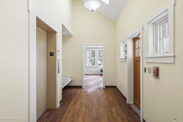 corridor with baseboards, high vaulted ceiling, dark wood-style flooring, and elevator