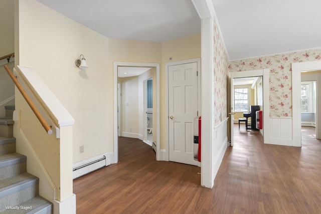 hallway featuring a baseboard heating unit, a wainscoted wall, dark wood-type flooring, stairs, and wallpapered walls