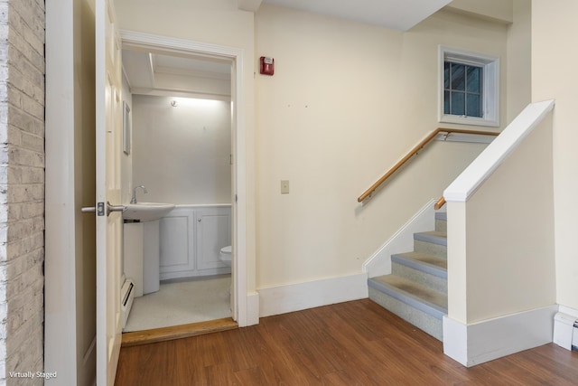 stairs with brick wall, baseboards, baseboard heating, and wood finished floors