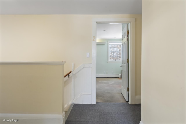 hallway with a baseboard heating unit, wainscoting, light carpet, and an upstairs landing