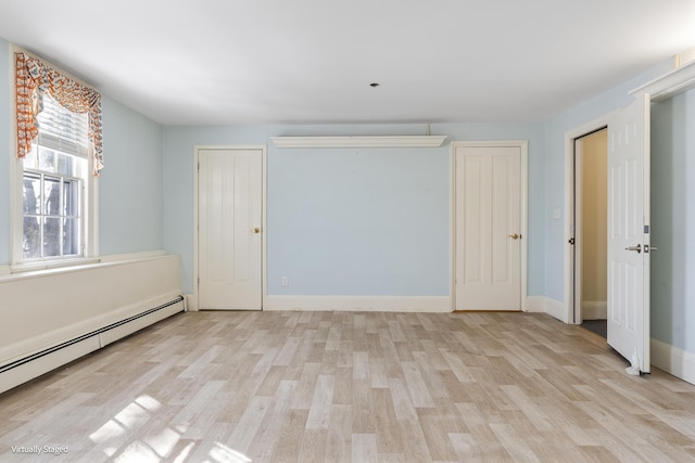 unfurnished bedroom with a baseboard heating unit, light wood-type flooring, and baseboards