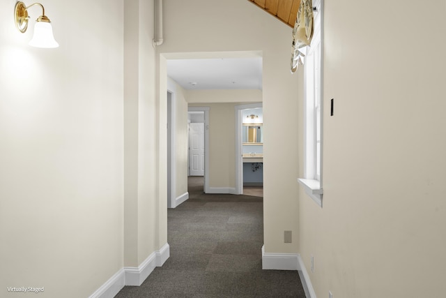 hall featuring dark carpet and baseboards