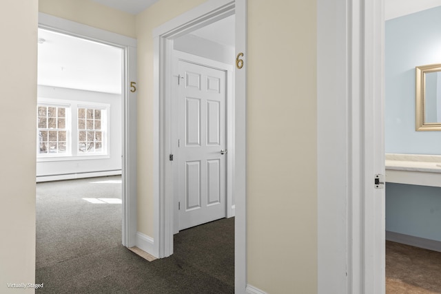 corridor featuring a baseboard heating unit, dark carpet, and baseboards