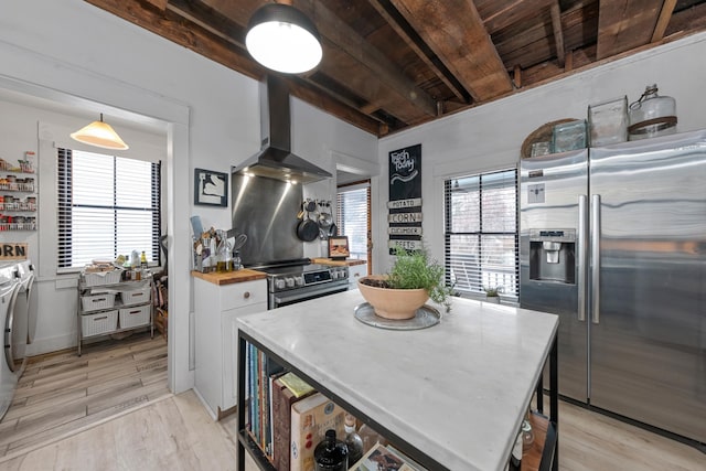 kitchen featuring light wood-type flooring, stainless steel appliances, wall chimney range hood, white cabinets, and washing machine and dryer