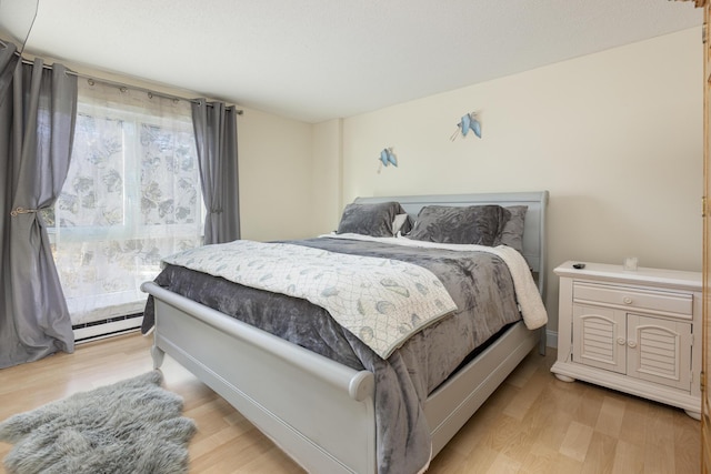 bedroom with a baseboard heating unit and light wood-type flooring