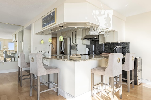 kitchen with light stone countertops, light hardwood / wood-style flooring, stainless steel appliances, wall chimney range hood, and decorative backsplash