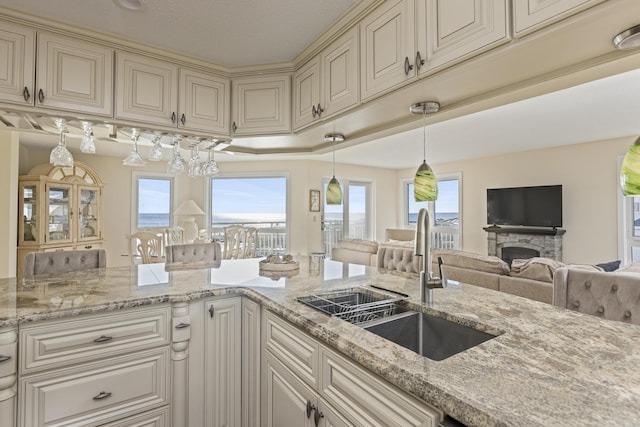 kitchen with light stone counters, cream cabinets, pendant lighting, a fireplace, and sink