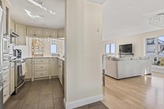 kitchen featuring stainless steel appliances, light wood-type flooring, cream cabinetry, and a textured ceiling