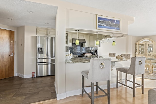 kitchen featuring cream cabinetry, stone counters, stainless steel refrigerator with ice dispenser, sink, and backsplash