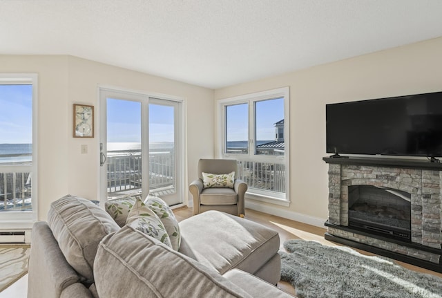 living room featuring a water view, hardwood / wood-style flooring, a baseboard heating unit, and a stone fireplace