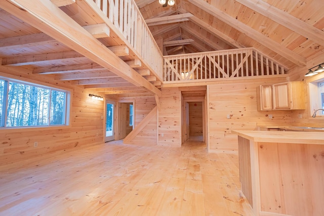 unfurnished living room with lofted ceiling with beams, wood ceiling, light wood-style flooring, wood walls, and a sink