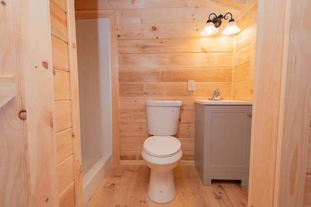 bathroom featuring toilet, wood walls, vanity, a shower, and wood-type flooring