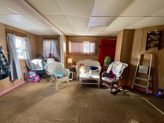 sitting room featuring a paneled ceiling, dark carpet, and wood walls