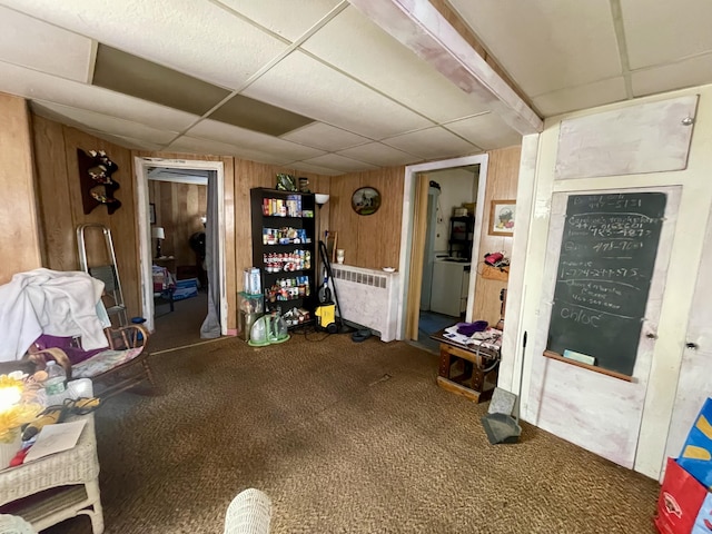 interior space featuring carpet flooring, a paneled ceiling, wood walls, and radiator