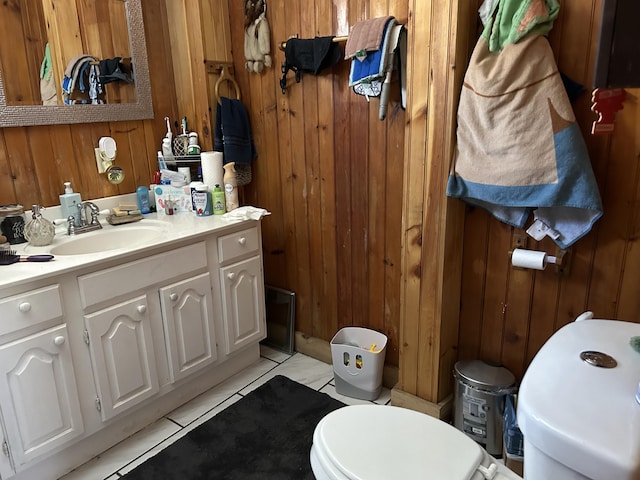 bathroom featuring tile patterned flooring, vanity, toilet, and wood walls