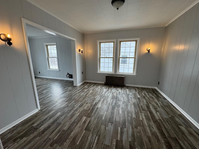 unfurnished room featuring radiator heating unit, wooden walls, dark wood-type flooring, and ornamental molding