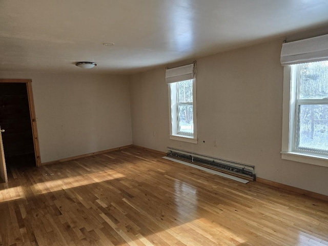 empty room with plenty of natural light, light wood-type flooring, and a baseboard heating unit