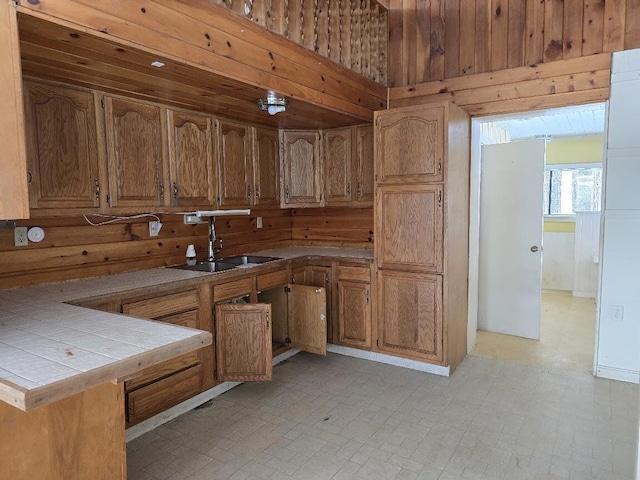 kitchen with kitchen peninsula, tile counters, sink, and wooden walls