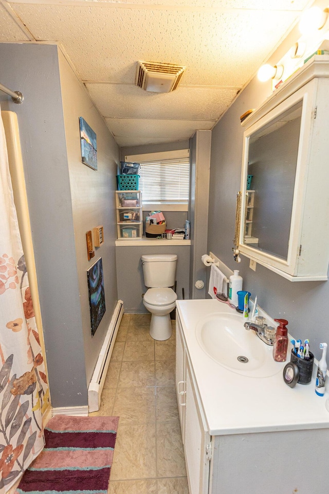 bathroom with a paneled ceiling, toilet, vanity, and a baseboard heating unit