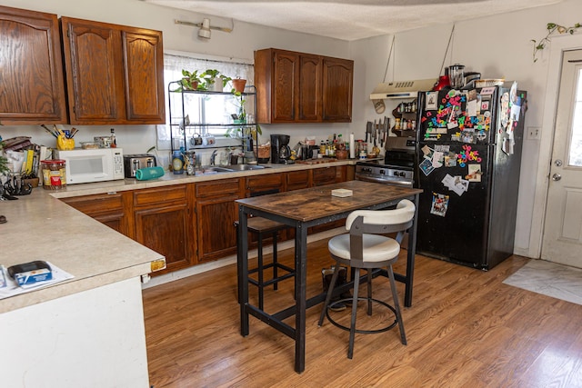 kitchen featuring sink, range hood, a textured ceiling, appliances with stainless steel finishes, and hardwood / wood-style flooring