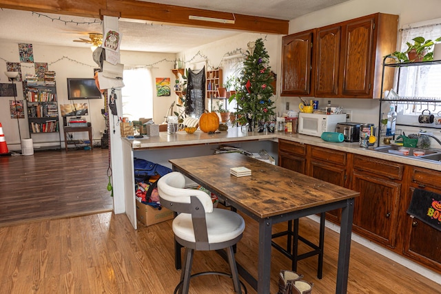 kitchen featuring plenty of natural light, beam ceiling, light wood-type flooring, and sink