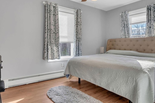 bedroom featuring ceiling fan, hardwood / wood-style floors, multiple windows, and a baseboard heating unit