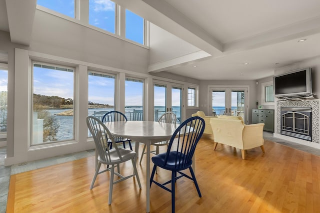 dining space with a fireplace, french doors, light hardwood / wood-style floors, and beamed ceiling