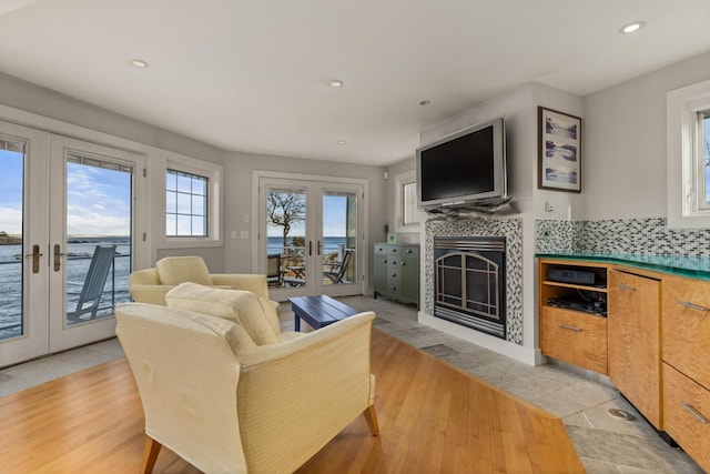 living room with a tile fireplace, french doors, a water view, and light hardwood / wood-style flooring