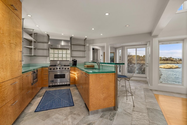 kitchen with sink, wall chimney exhaust hood, appliances with stainless steel finishes, kitchen peninsula, and a breakfast bar area