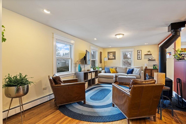 living room featuring baseboard heating, a wood stove, and hardwood / wood-style floors