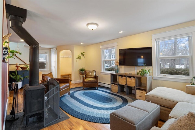 living room featuring hardwood / wood-style flooring, a baseboard heating unit, a healthy amount of sunlight, and a wood stove