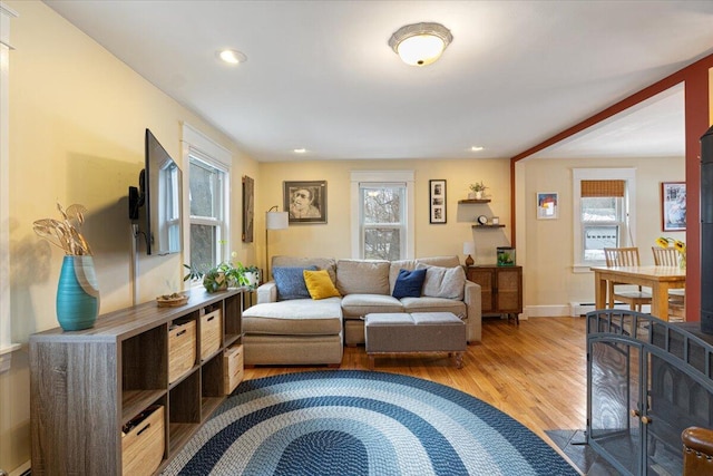 living room with baseboard heating, light wood-type flooring, and a healthy amount of sunlight