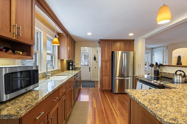 kitchen featuring hardwood / wood-style floors, stainless steel appliances, light stone counters, sink, and decorative light fixtures