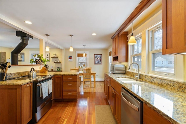 kitchen featuring decorative light fixtures, light hardwood / wood-style floors, a wood stove, appliances with stainless steel finishes, and sink