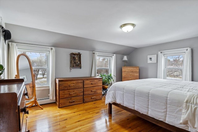 bedroom with vaulted ceiling, baseboard heating, multiple windows, and light hardwood / wood-style floors