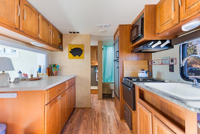 kitchen with sink, black appliances, extractor fan, and light wood-type flooring