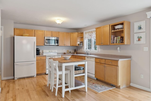 kitchen featuring white appliances, sink, light hardwood / wood-style floors, a kitchen island, and a breakfast bar area