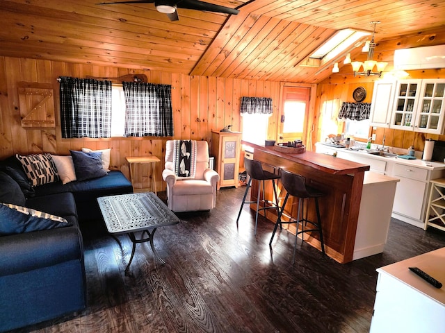 living room featuring wooden ceiling, ceiling fan with notable chandelier, wooden walls, vaulted ceiling with skylight, and dark hardwood / wood-style flooring