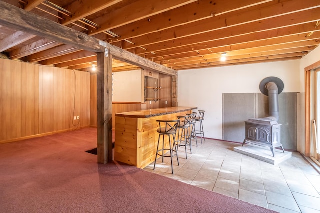 basement featuring a wood stove, bar area, tile patterned floors, and wooden walls