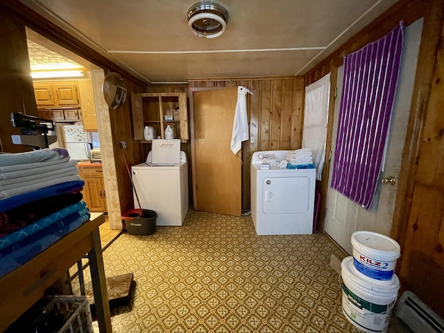 clothes washing area with a baseboard radiator, washer and clothes dryer, and wood walls