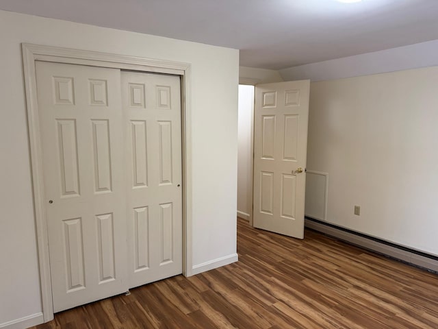 unfurnished bedroom with a baseboard heating unit, a closet, and dark wood-type flooring