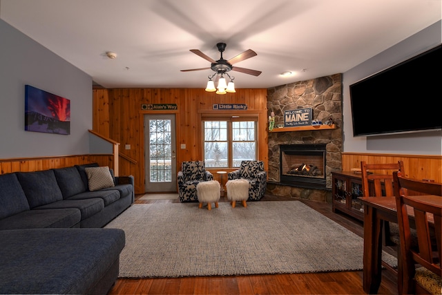 living room featuring a stone fireplace, ceiling fan, wooden walls, and hardwood / wood-style flooring